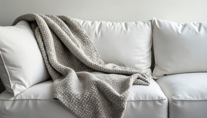 Stylish white sofa with a textured gray blanket draped over it in a minimalist living room.