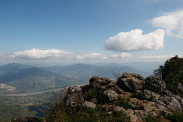 Scenic rocky outcrop overlooking vast green valleys and distant mountains under a bright blue sky in Phu Chi Fa National Park, ChiangRai, Thailand. 24 Jan 2017