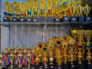 Golden trophies with black bases neatly arranged in a glass display case, representing success,...
