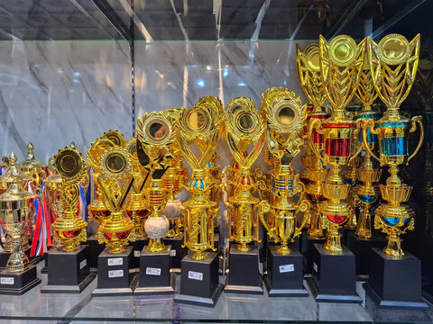 Golden trophies with black bases neatly arranged in a glass display case, representing success, achievement, championship, competition, and sports excellence.