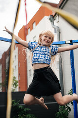 Blonde girl joyfully jumping in front of a colorful building.