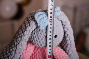 Soft knitted bunny toy with a measuring tape placed on its head.