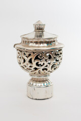 A small, ornate, silver-colored metal object with a detailed filigree design, isolated on a clean...