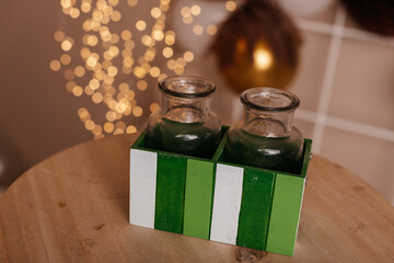 Two decorative glass vases placed beside a green gift box with festive lights.