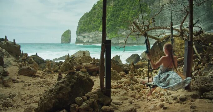 Woman swinging by the Sea. Tourist enjoying vacation on Tembeling Beach and Forest, Bali, Nusa Penida, Indonesia.