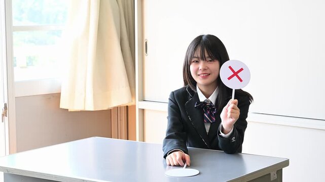 クイズに答える女子学生　学校の教室で○✕を出す教育イメージ