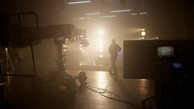 Silhouette of a man standing on a foggy studio set, dramatically backlit by bright golden lights, conveying themes of leadership, mystery, and cinematic production