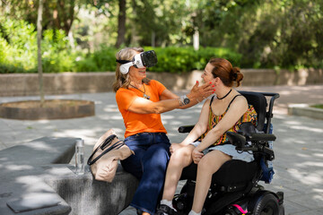 Senior woman sharing virtual reality experience with disabled girl in wheelchair in park