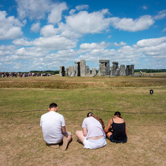 teenagers and mobile phones near ancient ruins of stonehenge under blue sky