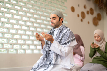 Fototapeta premium Muslim man wearing kufi in peaceful home praying with open hands in dua devotion, islamic faith worship mindfulness calm moment of religious connection, calm belief ramadan, eid religious tradition
