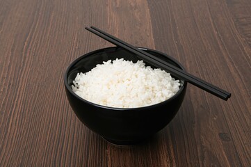 A black bowl filled with white rice and topped with black chopsticks