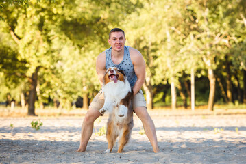 Lifestyle fun photo of athletic looking slavic man hugging his happy red merle australian shepherd...