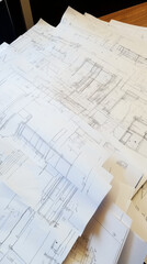 Architectural drawings and blueprints spread across a table. Detailed plans for construction or engineering projects.