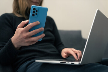 Woman holding a phone next to laptop. Concept of multitasking, connection and modern digital lifestyle. It suggests the integration of mobile technology and personal computing in everyday productivity