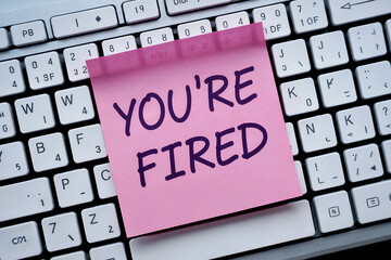 Pink sticky note with Y O U' R E F I R E D text on a computer keyboard you're fired