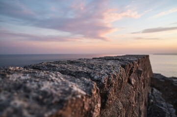 Obraz premium A textured rock barrier sharply captured, set against a soft pastel-hued sky and ocean backdrop during twilight.