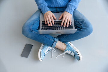 Person sitting cross-legged on floor typing on laptop with phone nearby image