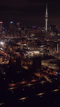 Auckland, New Zealand cityscape at night. The Sky Tower dominates the skyline, surrounded by illuminated buildings. The ASB building is visible, adding to the urban landscape.