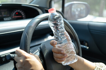Asian woman driver hold cold water for drink in car, dangerous and risk an accident.