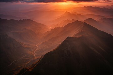 Sunset sunrays light up shadowy mountain slopes with foggy valleys and blurred peaks at dusk