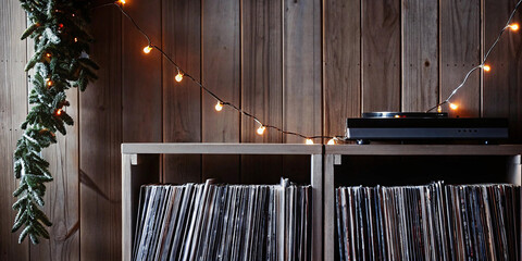 Warm toned christmas lights illuminating record player and vinyl records on rustic wooden shelf creating nostalgic seasonal background for music-themed holiday marketing content.