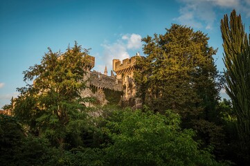 A medieval fortress surrounded by vibrant foliage beneath a clear sunny sky.
