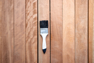 Top view of paint brush tool on pile of lumber, representing construction material and equipment used for improvement, protection or coating of wood grain surfaces. Visuals related to woodworking.