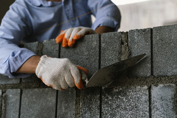 A skilled bricklayer works with mortar and trowel, carefully building a brick wall at a construction site with strength and precision.