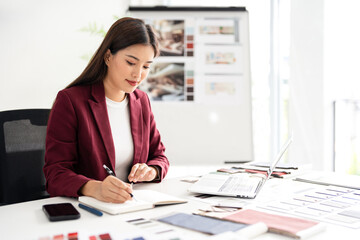 Interior designer working on her project  in studio office holding pen taking notes in a notepad .