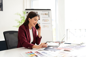 Designer working in office and making call on mobile phone. Female interior designer talking by...