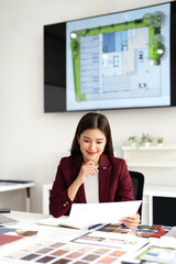 Smiling asian woman interior designer sit at modern office desk considering document in morning....