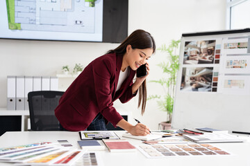 Concentrated young interior designer woman at table with blueprint drawing ,swatches and material ,...