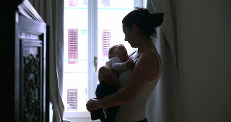 Mother kisses her sleeping baby on the head, showing love and affection while standing by the...