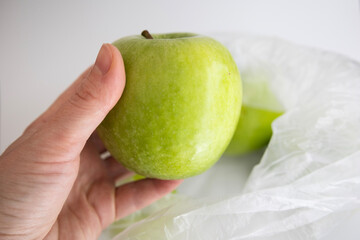 Hand holding green organic apple above transparent recycled eco bag with fresh apples isolated on...