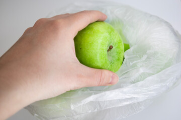 Hand placing green organic apple into transparent recycled eco bag with fresh apples isolated on...