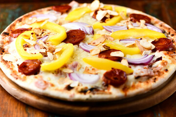 Pizza with chorizo ​​sausage, mozzarella cheese and yellow pepper. Rustic wooden background. Soft focus.	