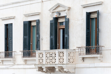 The fa ade of a white building with green shutters and a decorative balcony.