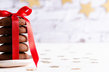 Cropped stacked chocolate cookies tied with a red ribbon and a garland of golden stars at the back....