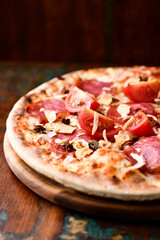 Pizza with salami, tomatoes and mozzarella cheese. Rustic wooden background. Soft focus. Copy space.	