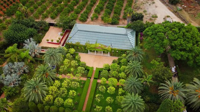 Drone video shows a lush public garden in Spain, with structured greenery, a pool, and architectural elements surrounded by orchards and scenic landscapes.