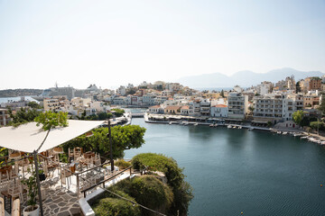 Panoramic view of Agios Nikolaos harbor in Crete with boats and a seaside restaurant terrace