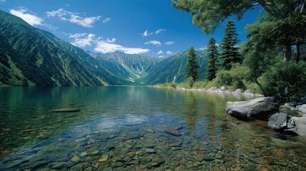 Fototapeta premium Tranquil lake surrounded by lush green mountains beneath a clear blue sky with scattered clouds, serene natural beauty