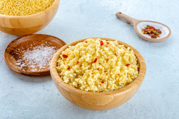 Cooked millet, ancient African grain, in a wooden bowl on a blue background, with salt and pepper. Healthy vegan side dish