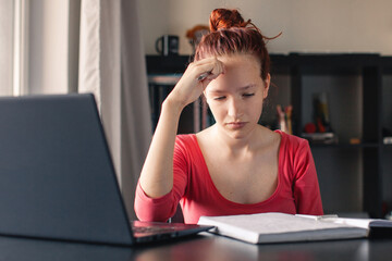 Sad and tired student girl looking on laptop and notebook
