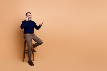 Successful mature businessman in formal attire chatting on mobile phone while seated on a wooden...