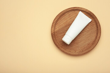 White cosmetic tube on wooden plate on beige background.