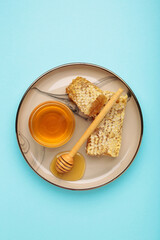 Bowl of sweet honey, dippers and combs on plate on blue background. Vertical photo