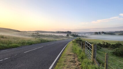 Empty rural road through misty fields at sunrise, wide calm sky