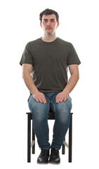 Full length portrait of casual young man sitting on a chair, hands on knees, looking serious to...