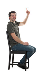 Side view casual guy seated on a chair pointing up forefinger, looking contented to camera. Happy man full length portrait isolated on transparent background
